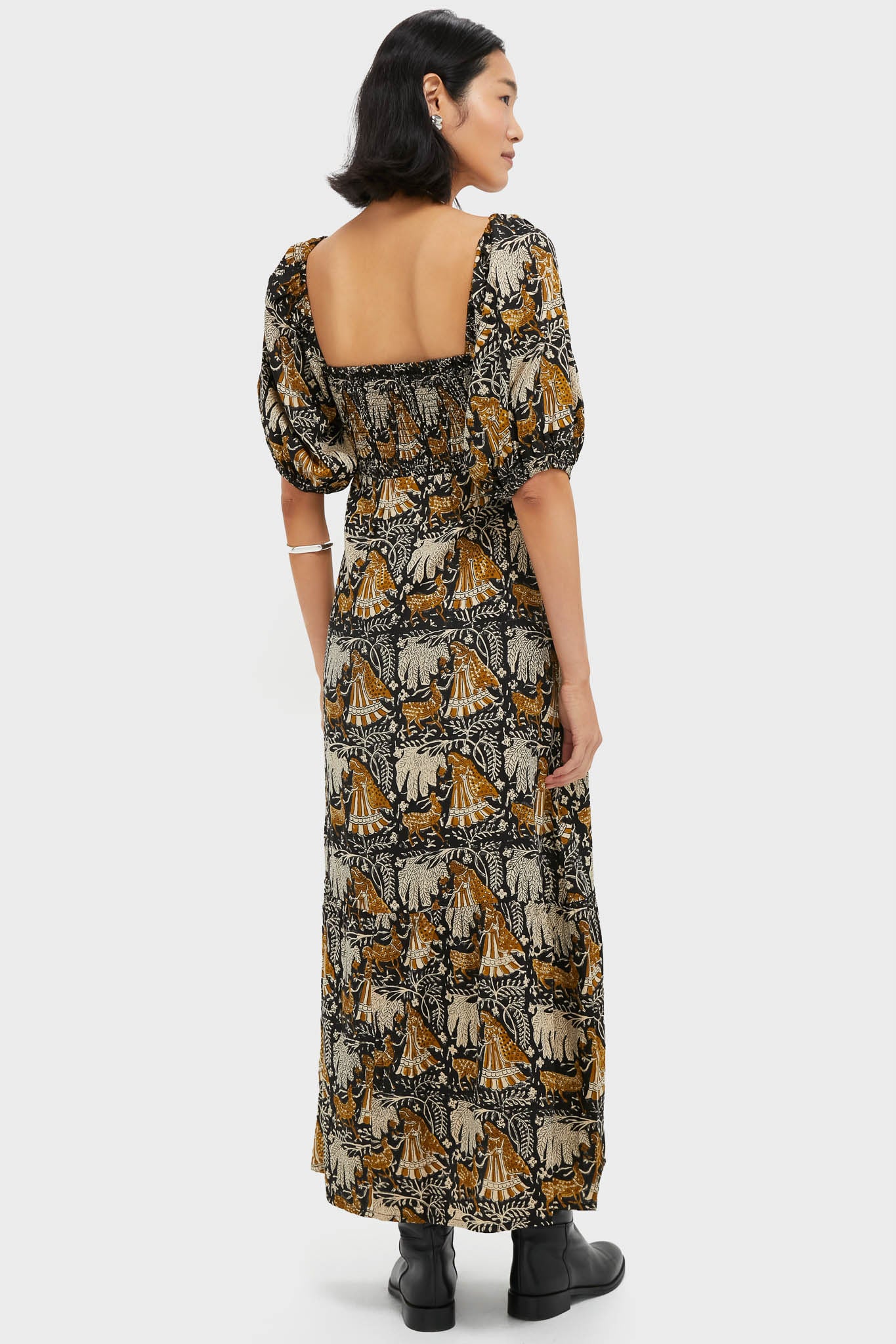 Back view of a woman in the Story Print Santiago 3 Maxi Dress, featuring a classic, effortless silhouette with puff sleeves and an open back, styled with black ankle boots.