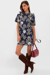 Model wearing the Navy Floral Mimi Mini Dress with classic puff sleeves and ruffle collar, paired effortlessly with dark brown knee-high boots and a burgundy crossbody bag.