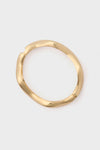 A gold, sculptural cuff-style round bangle from Petit Moments with a slightly irregular shape.