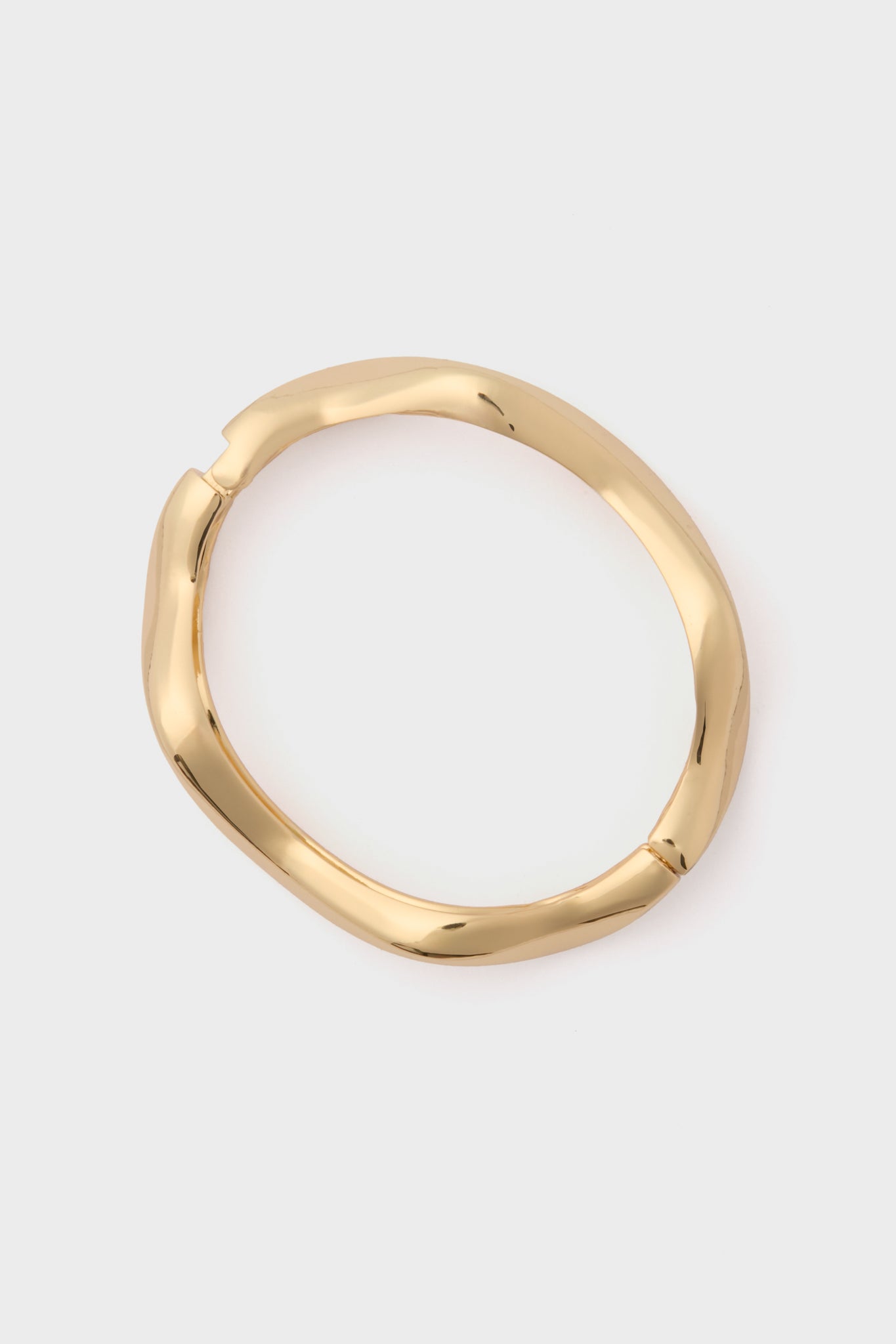 A gold, sculptural cuff-style round bangle from Petit Moments with a slightly irregular shape.