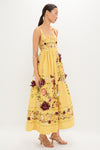 Woman models the Paramo Barbara Maxi Dress, a classic, high-end sundress with an effortless full skirt, warm yellow floral print, and square-neck bodice, embodying fun sophistication.