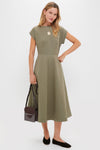 Model in olive midi dress wearing Gold Jumbo Bonne Chance Coin Necklace, exuding effortless elegance. Accessorized with classic flats and a chic shoulder bag for a high-end, fun look.