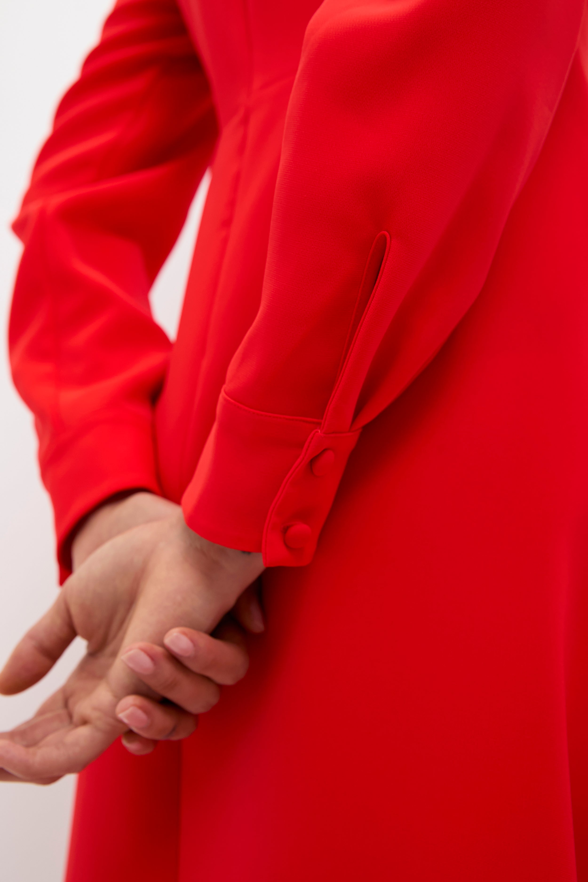 Close-up of hands clasped behind back, showcasing the Red Delancey Dress with classic banded cuffs and fabric-covered buttons, embodying effortless high-end elegance for holiday fun.