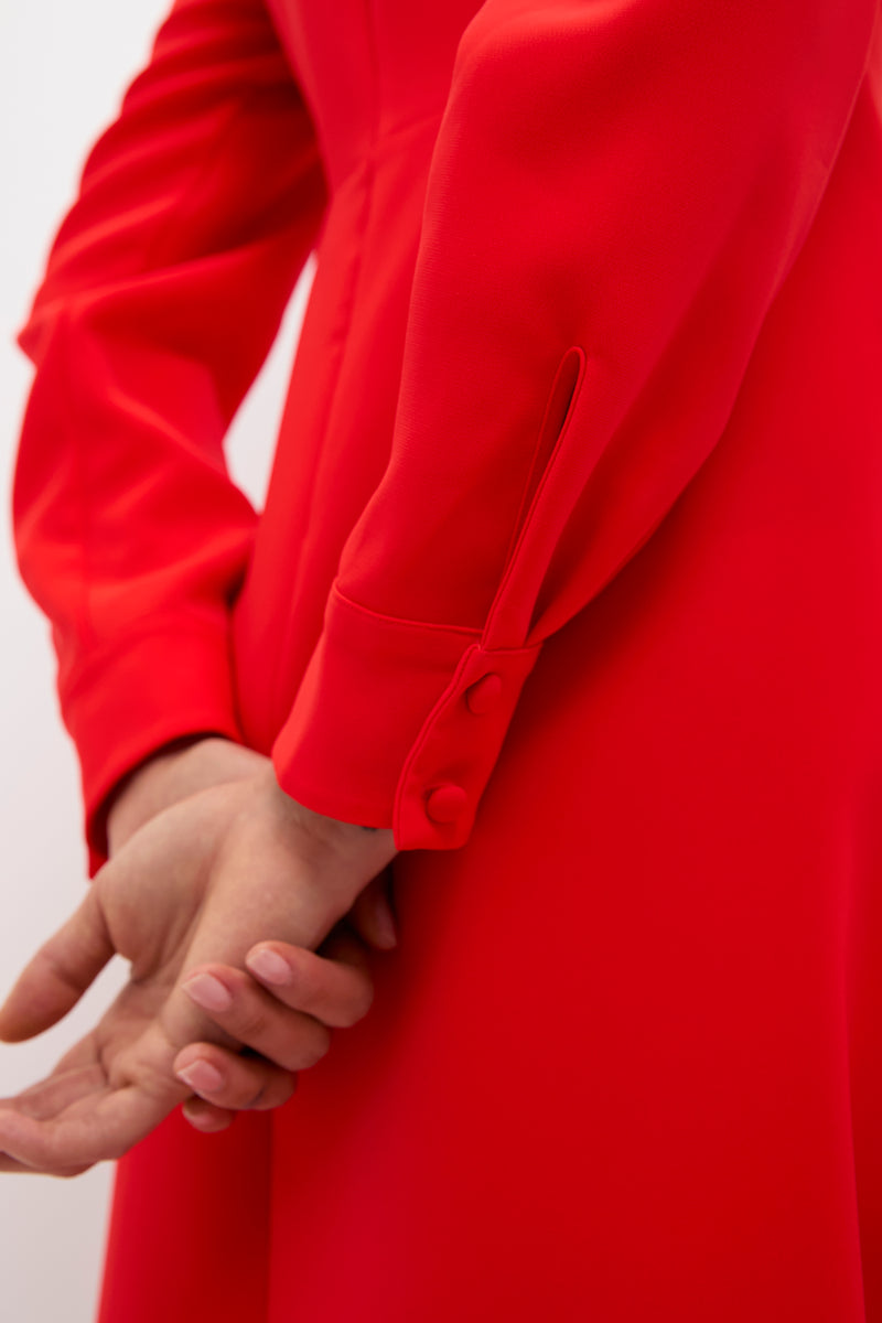 Close-up of hands clasped behind back, showcasing the Red Delancey Dress with classic banded cuffs and fabric-covered buttons, embodying effortless high-end elegance for holiday fun.