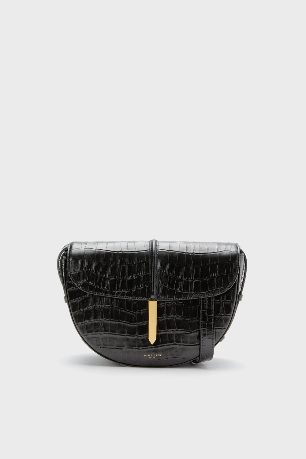 The Demellier Black Croc Tokyo Saddle Bag is a handcrafted leather crossbody handbag with a crocodile pattern and gold clasp, offering an elegant design.