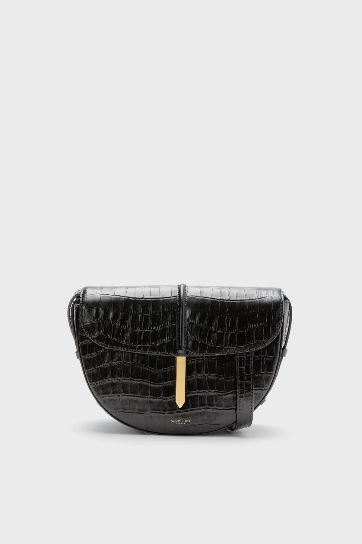 The Demellier Black Croc Tokyo Saddle Bag is a handcrafted leather crossbody handbag with a crocodile pattern and gold clasp, offering an elegant design.