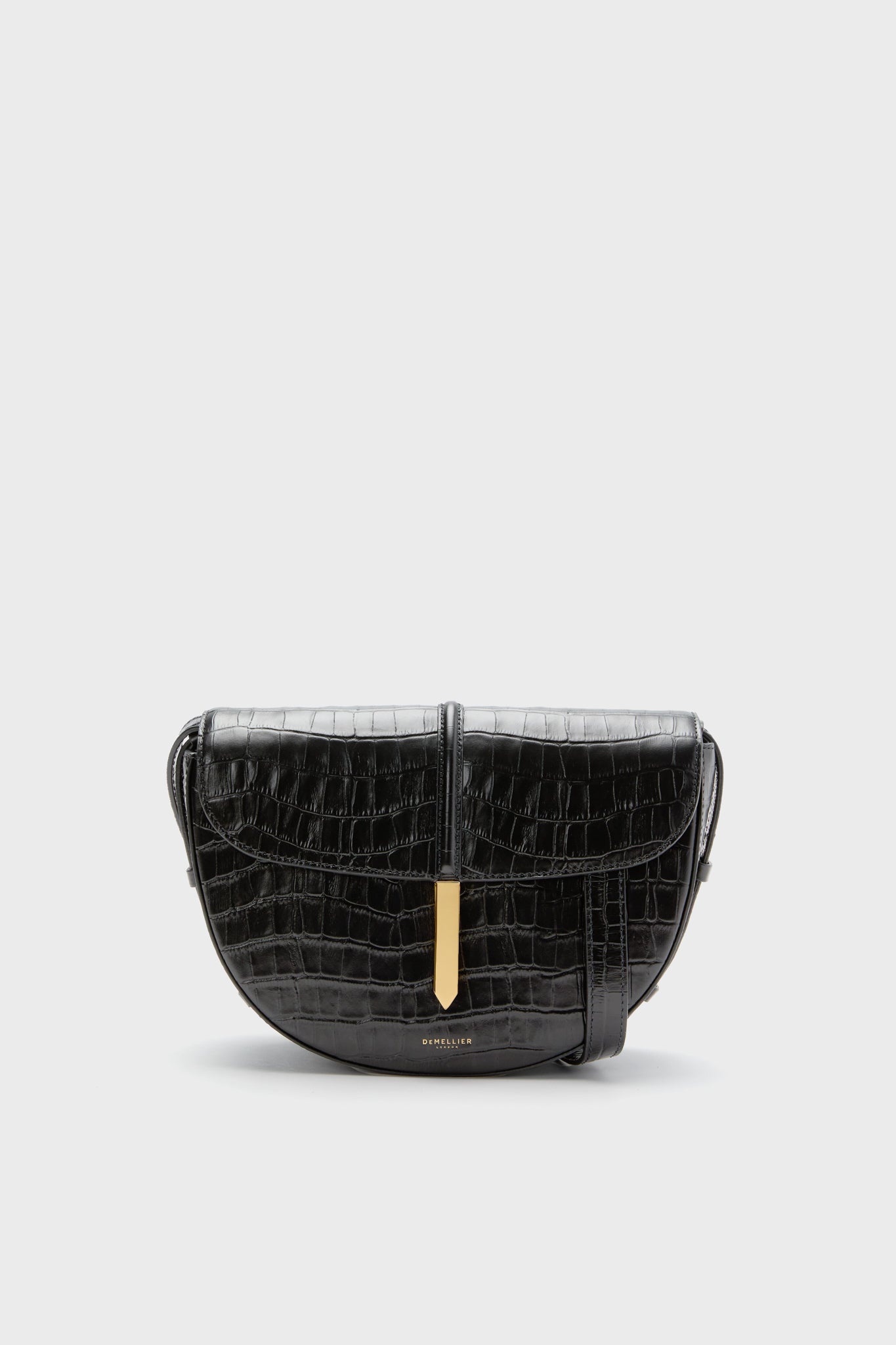 The Demellier Black Croc Tokyo Saddle Bag is a handcrafted leather crossbody handbag with a crocodile pattern and gold clasp, offering an elegant design.