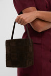 Person holding the Woven Tmoro Suede Laith Top Handle Bag, featuring a classic espresso suede weave and effortless drawstring design, epitomizing high-end, fun style.