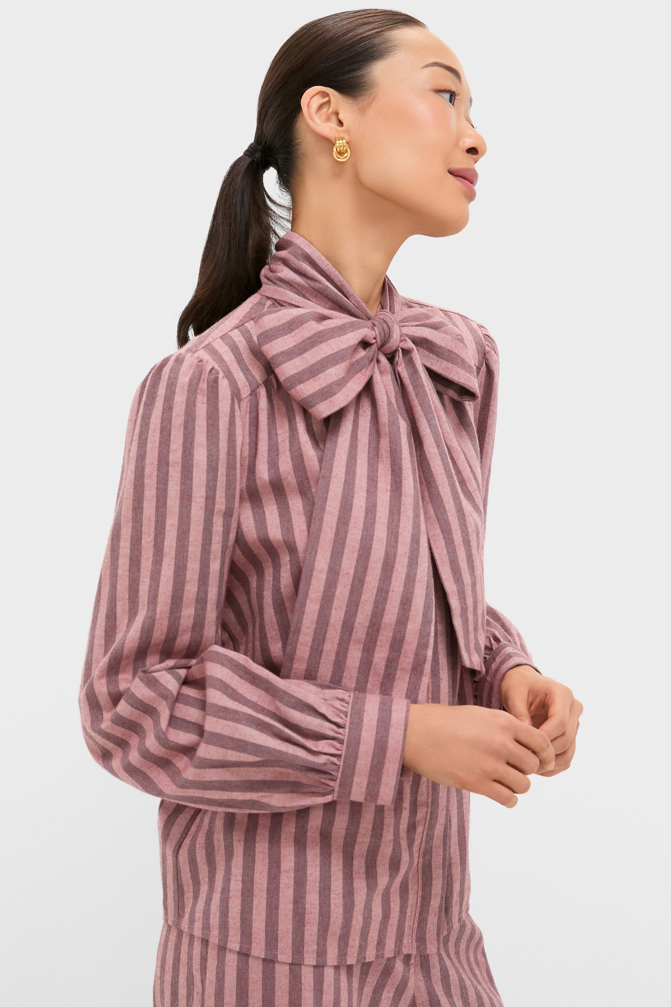 Model wearing Mauve Stripe Brianna Bow Blouse with an oversized bow, blouson sleeves, and chunky gold hoops, showcasing a classic, effortless high-end style.