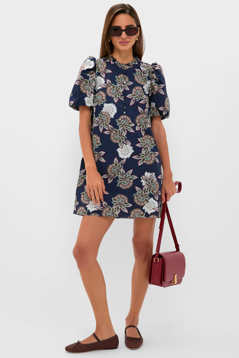 Woman in Navy Floral Mimi Mini Dress with puff sleeves, accessorized with dark sunglasses, gold hoop earrings, a burgundy crossbody bag, and brown ballet flats, exuding classic, effortless style.