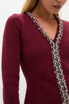 A woman wears a Hyacinth House burgundy knit mini dress with long sleeves, a V-neckline, and intricate silver bead and crystal embellishments.