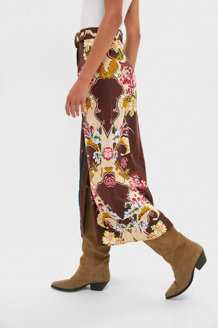 A person wearing the Anna Cate Portia Skirt—a long, floral print skirt with a side slit—paired with tan suede heeled boots and a white top.