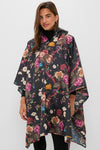 Someone wears a Barbour x Tuckernuck dark, packable floral poncho with a hood, standing against a plain light background.