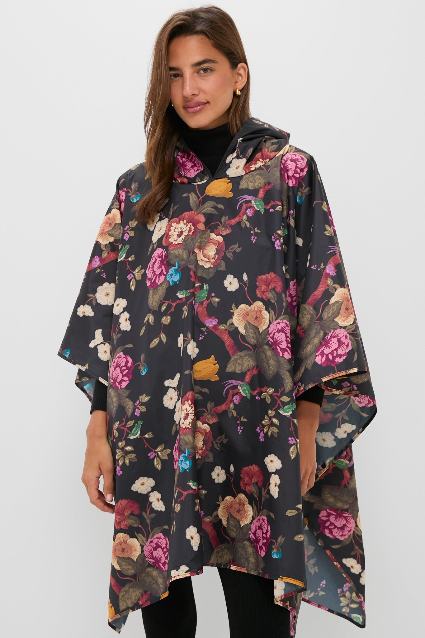 Someone wears a Barbour x Tuckernuck dark, packable floral poncho with a hood, standing against a plain light background.
