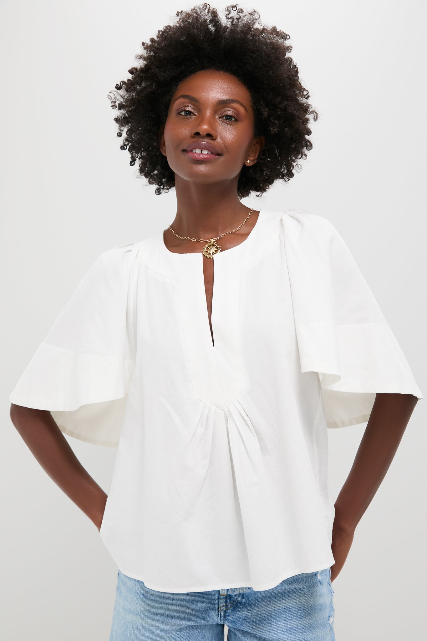 A woman wears a Pomander Place white cotton blouse with short flutter sleeves and a V-neckline, paired with light blue jeans.
