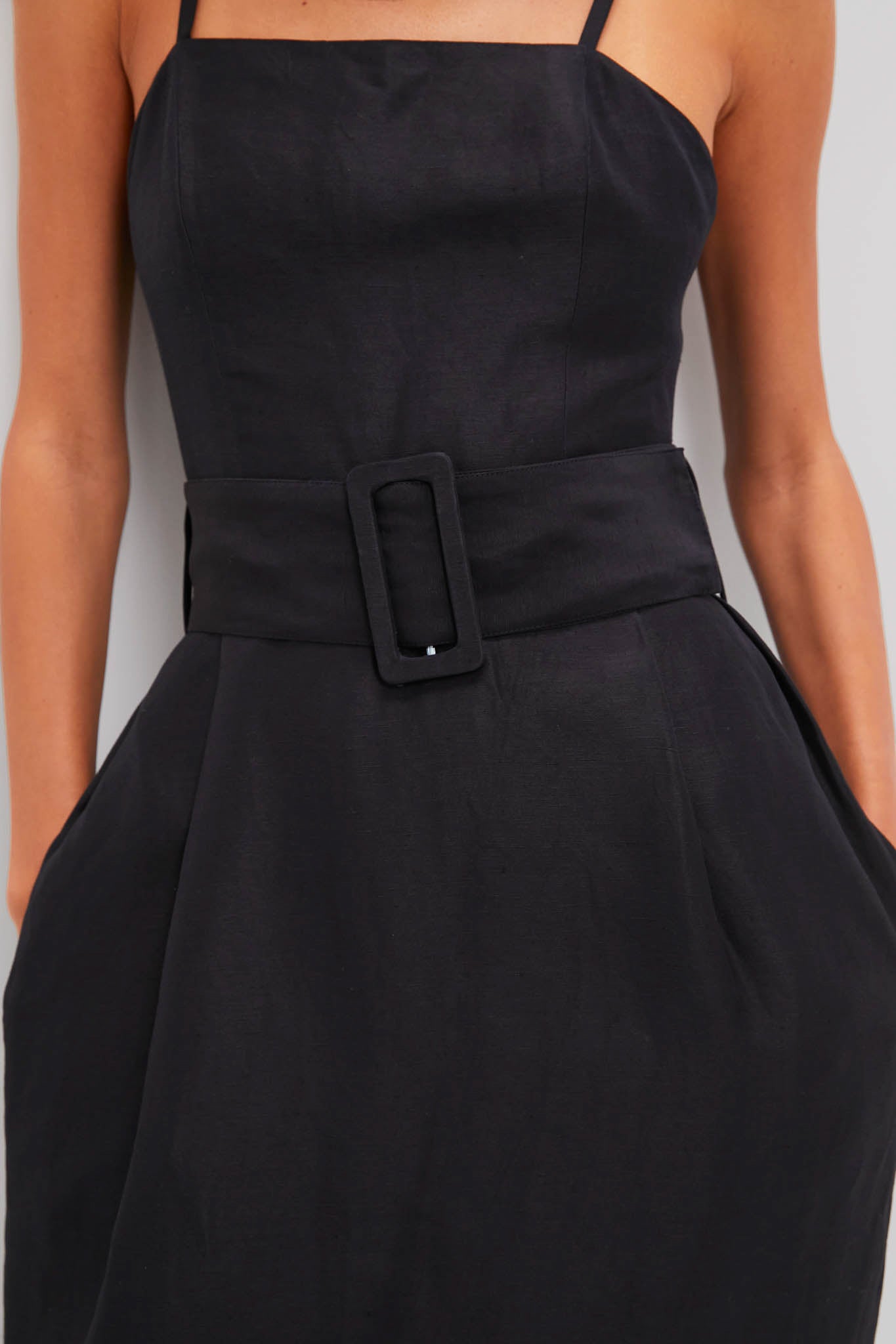 Woman in a Black Artichoke Dress with Belt, showcasing a classic, effortless look with a square neck, subtle pleats, and a bold, high-end statement belt.