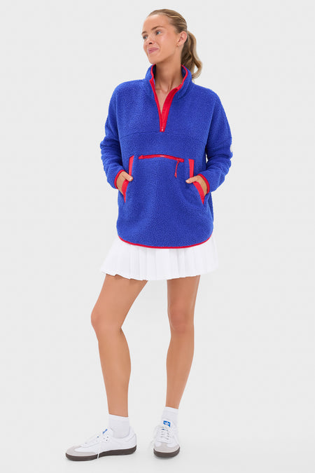 Female model in a classic, high-end Blue and Red Fleece Cady Quarter Zip with effortless style, featuring a kangaroo pouch and contrast trim, paired with a white mini-skirt.