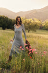 Woman in a blue sweater dress walking through flowers. 