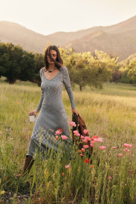 Woman in a blue sweater dress walking through flowers. 