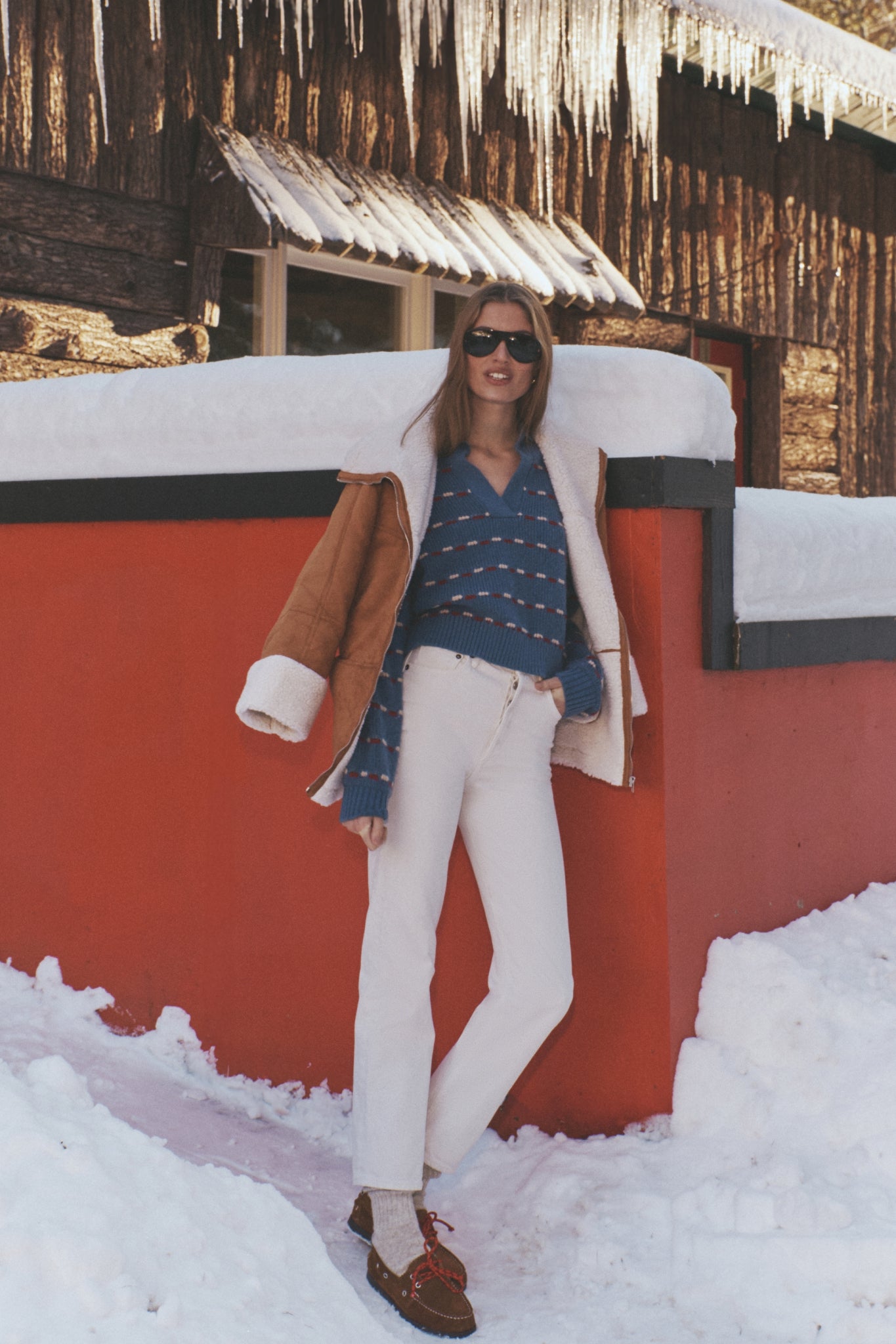 Young woman in a classic Navy Striped Jansen V-Neck Polo Sweater, styled effortlessly with off-white jeans and tan shearling jacket, exuding high-end winter fashion.
