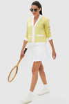 Woman in Lemongrass Cable Charley Cardigan with pleated skirt and sneakers, showcasing a classic, effortless, and fun high-end tennis-inspired look.