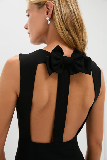 A woman wears a sleeveless black maxi dress by Hyacinth House, featuring an open back and statement neckline bow, paired with drop earrings—an elegant look for any evening event.
