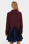 A woman faces away from the camera in a Tuckernuck long-sleeve burgundy shirt featuring black and navy scalloped patterns, a ruffled navy hem, and the playful swing silhouette of a flouncy mini dress.