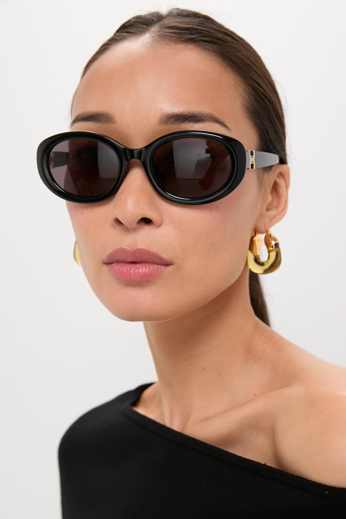 Woman in sleek Shiny Solid Black Marcie Sunglasses with chunky gold hoops, exuding a classic, effortless, and high-end style. Perfect for fun, versatile looks.