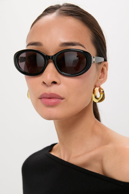 Woman in sleek Shiny Solid Black Marcie Sunglasses with chunky gold hoops, exuding a classic, effortless, and high-end style. Perfect for fun, versatile looks.