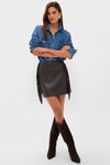 Woman modeling the Coffee Faux Faux Leather Fringe Paddock Mini Skirt; a classic, effortless look paired with a denim shirt and suede boots, exuding fun, high-end style.