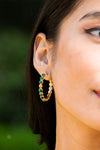 Berry Gem Medium Hoop Earrings - Malachite adorn a woman's ear, showcasing classic, effortless luxury with green stones and gold beads, embodying fun, high-end style.