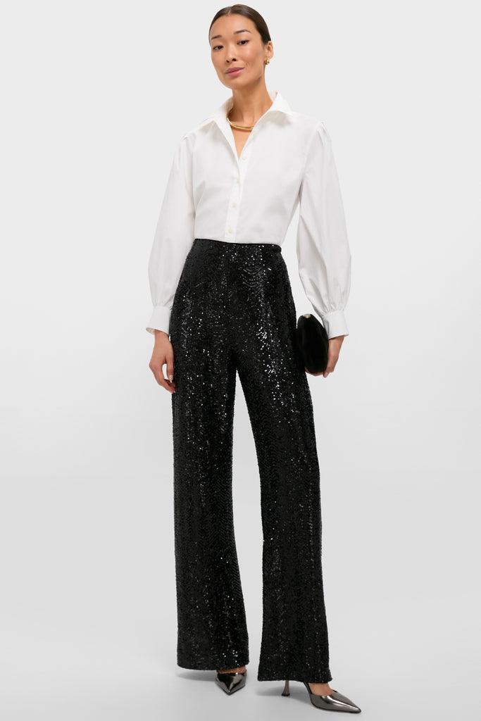 Woman in Black Sequin Tatum Pants paired with a classic white shirt, exuding effortless high-end style. She's accessorized with gold jewelry and a chic clutch.