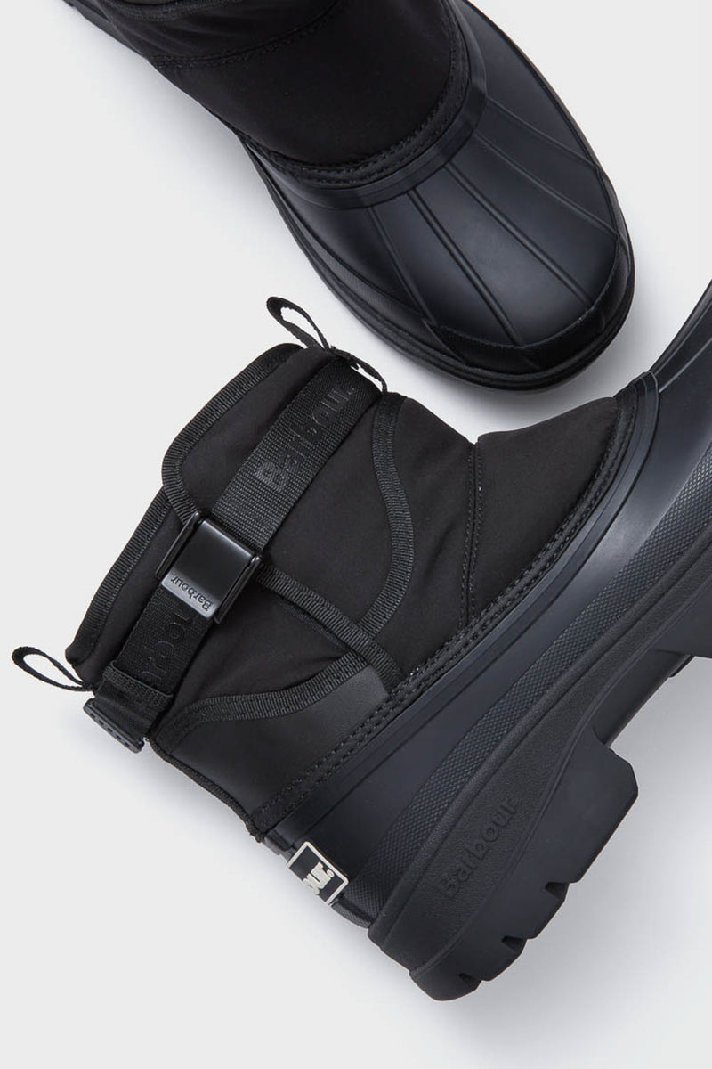 Two black Barbour waterproof winter boots with thick rubber soles and strap detail are displayed on a light gray background.