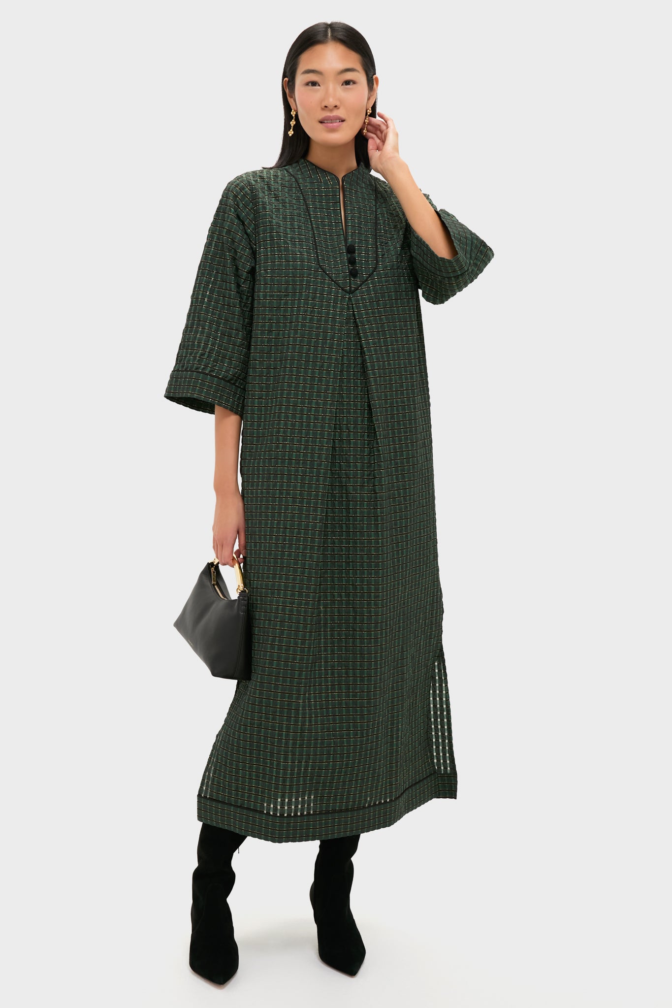 Model wearing the classic Metallic Green Plaid Indy Maxi Dress, featuring a relaxed silhouette and subtle sheen, paired with knee-high boots and gold accents for effortless, high-end style.