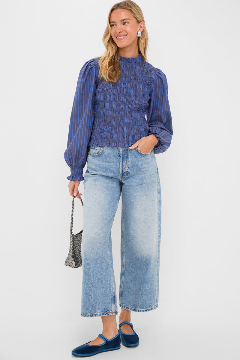 Woman modeling the Morgan Blue Willow Top, a classic, high-end blouse with smocked bodice and balloon sleeves, paired with light-wash jeans and fun accessories for an effortless look.