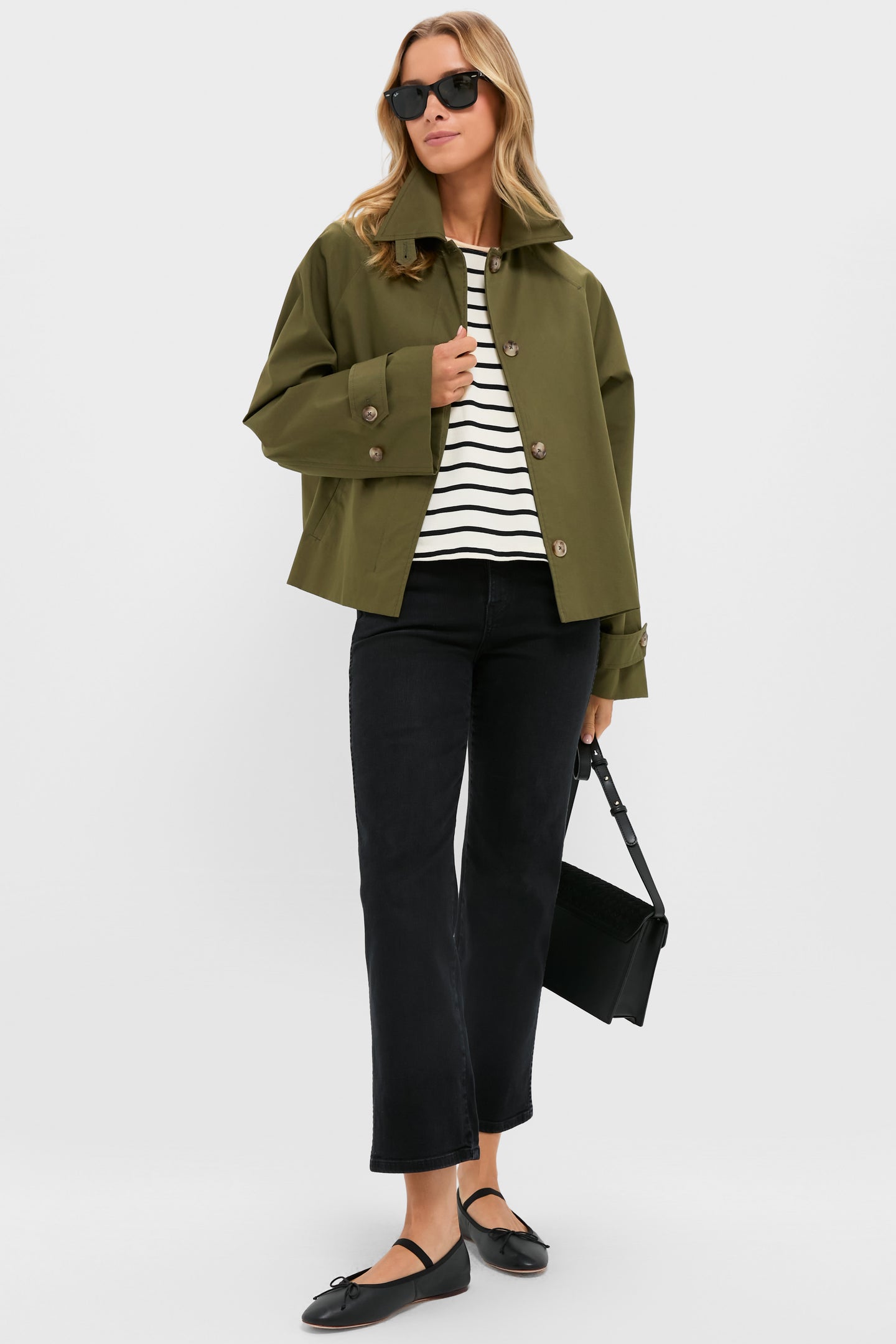 A woman in a Twin Doves Denim olive jacket, striped top, high-rise jeans, black flats, sunglasses, and holding a black handbag.