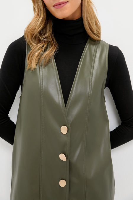 Model wearing the Olive Faux Leather Pinafore Dress with a V-neck and matte-gold buttons over a black turtleneck, embodying a classic and effortlessly high-end style.