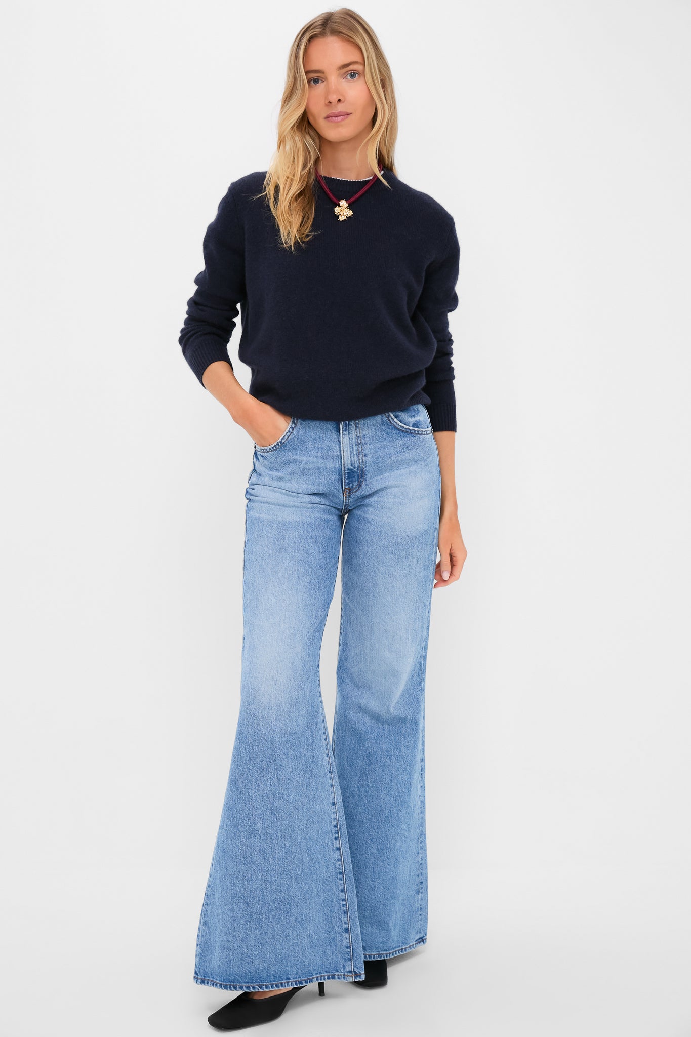 Woman wearing classic Blondie Vandam Jean with high-rise, slim fit, and fun wide-leg flare, styled effortlessly with a navy sweater and heels.