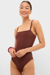 Young woman models the classic Cappuccino Isabel One Piece swimsuit with a square neck and thin straps, exuding an effortless, high-end style, accessorized with fun, chunky bangles.