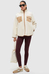 Woman in Buttercream Fleece Lawrence Full Length Zip Up, a classic sherpa jacket with chest pockets, paired with fitted leggings and sneakers for an effortless, high-end athleisure look.