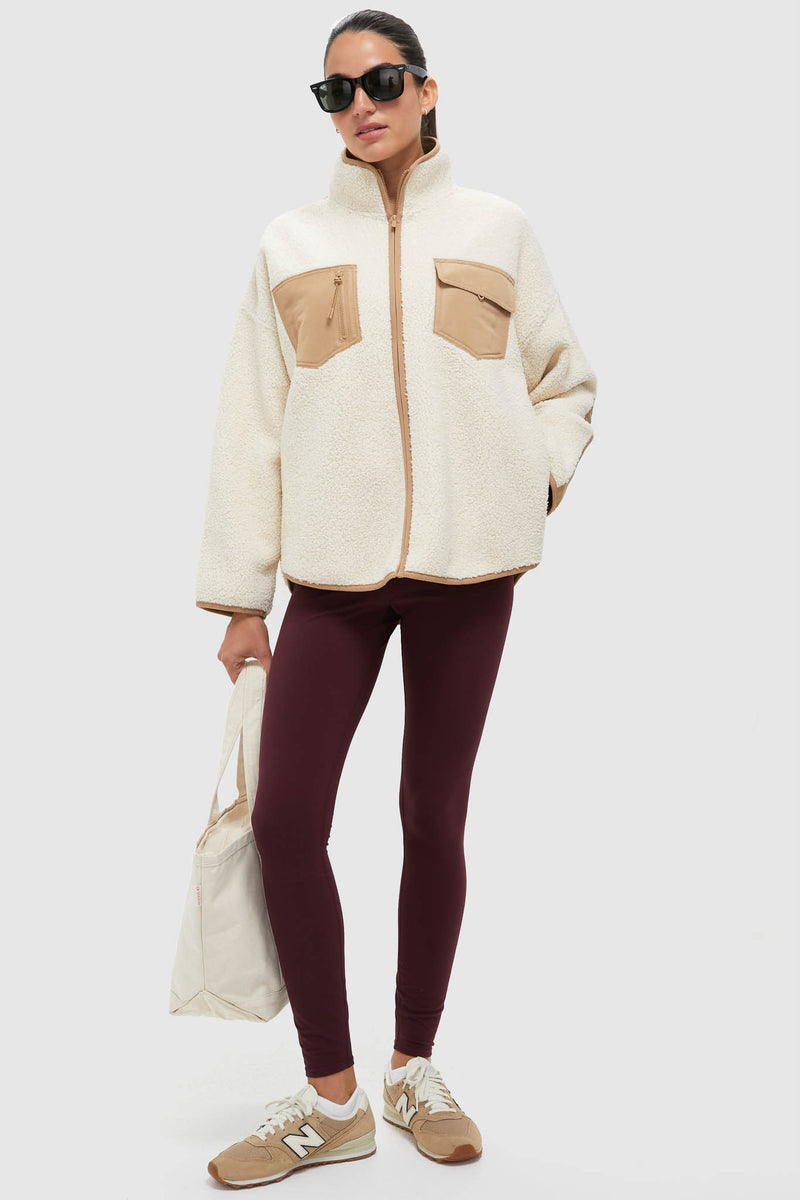 Woman in Buttercream Fleece Lawrence Full Length Zip Up, a classic sherpa jacket with chest pockets, paired with fitted leggings and sneakers for an effortless, high-end athleisure look.