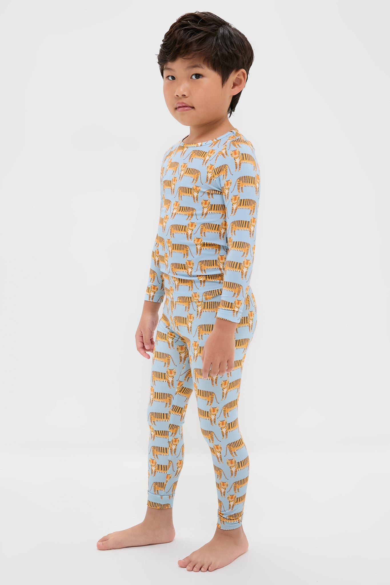 Young boy in classic, effortless Tigers Kids Bamboo Pj Set, featuring fun tiger prints on a light-blue top and leggings. High-end, breathable bamboo fabric ensures comfort.