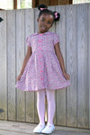 Young girl in a classic, effortless Pink Floral Button Front Dress, featuring a Peter Pan collar, puff sleeves, and pink buttons, embodying high-end, fun style.