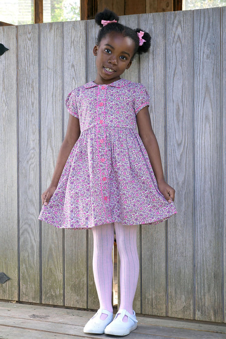 Young girl in a classic, effortless Pink Floral Button Front Dress, featuring a Peter Pan collar, puff sleeves, and pink buttons, embodying high-end, fun style.