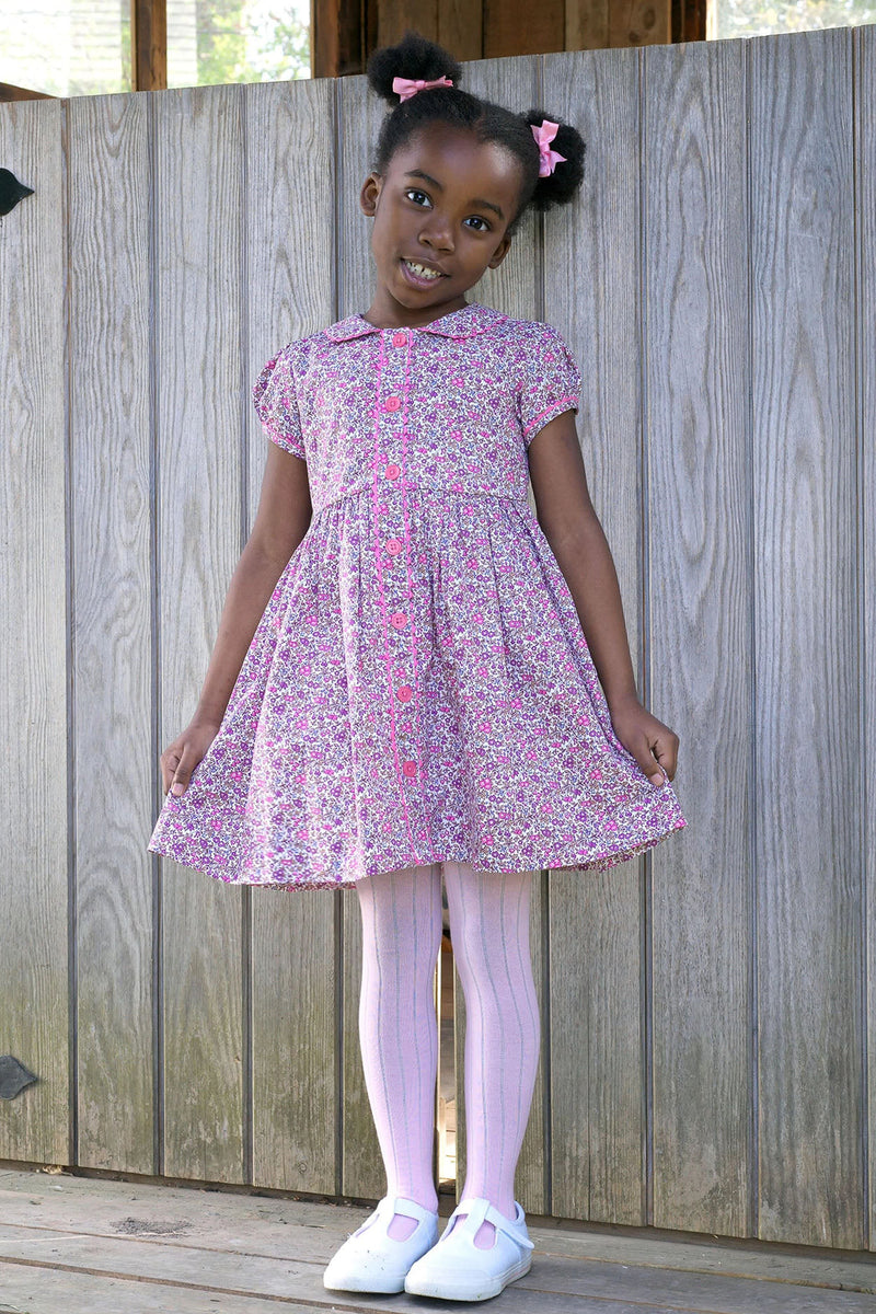 Young girl in a classic, effortless Pink Floral Button Front Dress, featuring a Peter Pan collar, puff sleeves, and pink buttons, embodying high-end, fun style.
