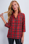 A woman wears a Tuckernuck red Royal Stewart Tartan Margot Top with a split collar and black pants.