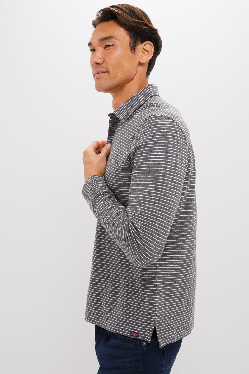 A man in a Faherty sunwashed polo with thin white stripes stands against a plain light background, facing sideways—highlighting timeless, sustainable style.