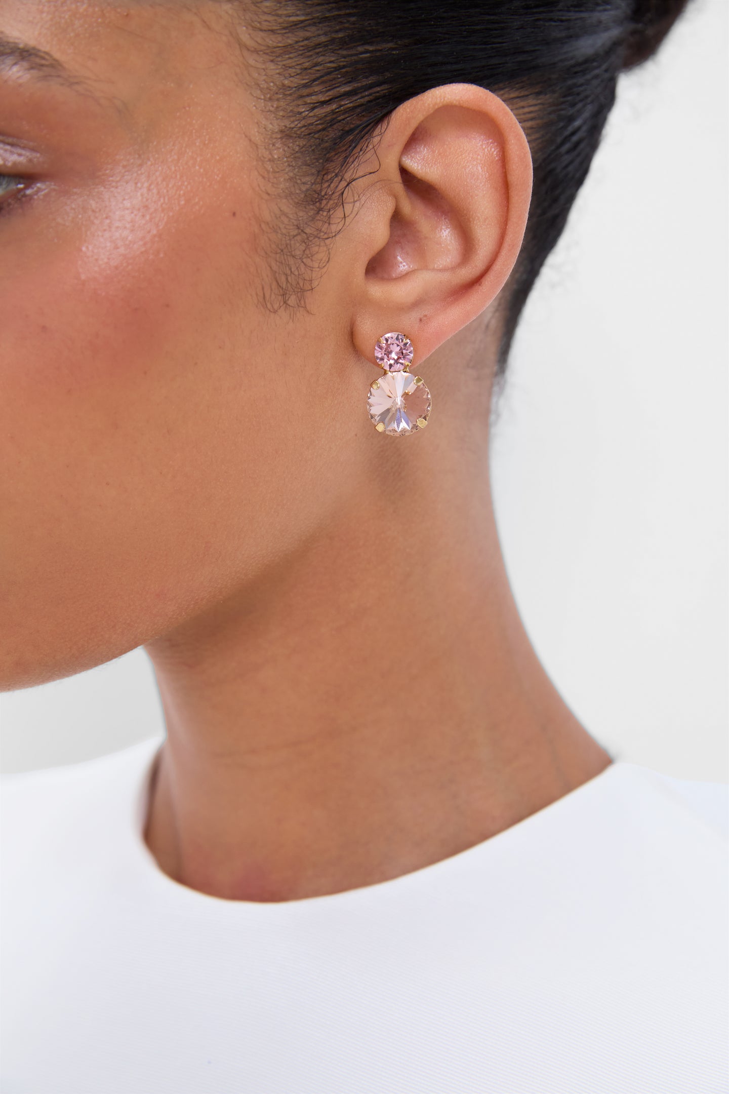 Close-up of a classic, high-end Rose Quartz Myrla Earrings, featuring effortless drop design with shimmering pink crystals set in gold-tone metal, worn with a white garment.