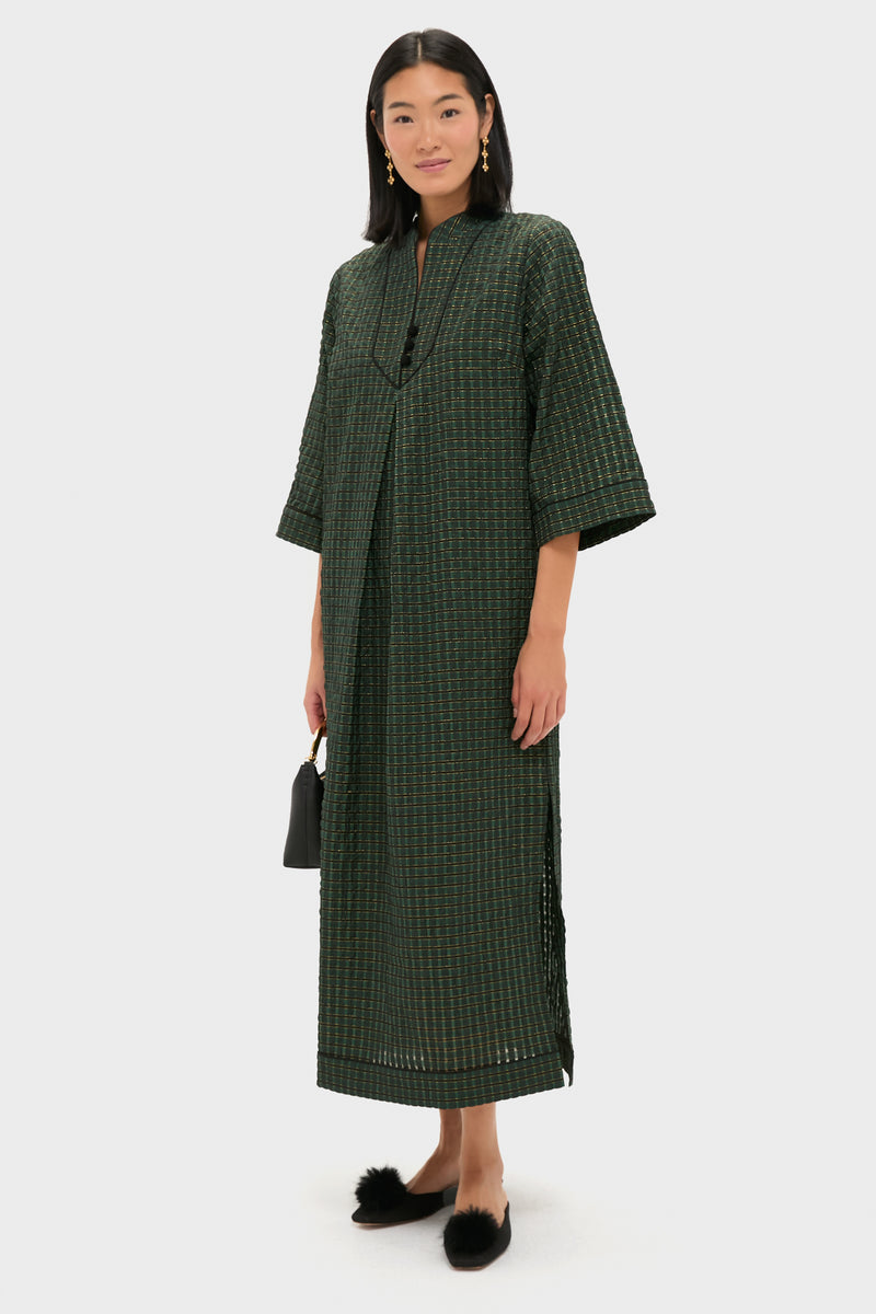 Model in the Metallic Green Plaid Indy Maxi Dress showcasing a classic, effortless look. Paired with a black handbag, pom-pom flats, and gold earrings for high-end fun.