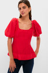 A woman stands confidently in a Hyacinth House ruby red, puff sleeve blouse with a square neckline and dark jeans.